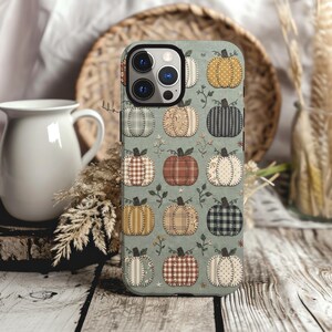 May include: A sage green smartphone case featuring a repeating pattern of pumpkins in various fabrics, including plaid, polka dot, and striped textures in shades of orange, brown, cream, and black, accented with small embroidered floral sprigs.