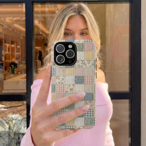 May include: A patchwork-style phone case featuring a mix of floral, gingham, and solid fabric squares in pastel colors. The case has a camera cutout and is held up in front of a person.