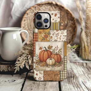 May include: A smartphone case featuring a patchwork design with autumn-themed patterns including orange pumpkins, white pumpkins, brown acorns, fall leaves, and floral motifs in shades of orange, brown, cream, and green with a triple camera cutout.