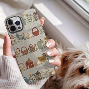 May include: A phone case featuring a light grey fabric-textured background with a repeating pattern of small houses, chickens, watering cans, baskets, eggs, and flowers in muted tones of brown, blue, green, yellow, and cream colours.