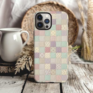 Puede incluir: Una funda para smartphone con un diseño de patchwork que presenta una cuadrícula de pequeños cuadrados en tonos pastel suaves de rosa, azul, amarillo y morado. El patrón incluye varias texturas como pequeños estampados florales, cuadros y lunares.