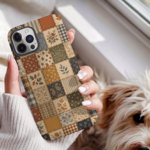 May include: A smartphone case featuring a patchwork design with various squares in muted earth tones. The pattern includes floral prints, leaves, paisley, stripes, and polka dots in shades of brown, cream, navy blue, and sage green.