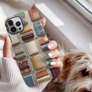 May include: A smartphone case featuring a repeating pattern of small, rectangular books with various fabric-like textures, including plaid, floral, polka dot, and solid prints in shades of blue, green, yellow, brown, and burgundy on a light background.