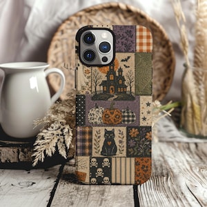 May include: A smartphone case featuring a patchwork design with Halloween-themed illustrations including a haunted house, pumpkins, a black cat with a heart, skulls, bats, and floral patterns in shades of orange, purple, black, and cream.