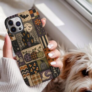 May include: A smartphone case featuring a patchwork design with Halloween motifs including a haunted house, pumpkins, ghosts, candy corn, a tombstone with the text RIP, a skeleton, a black cat, bats, and a crescent moon in orange, black, and purple.