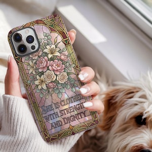 May include: A phone case featuring a stained glass style design with a bouquet of pink and white flowers, green leaves, and an arched border. The text "SHE IS CLOTHED WITH STRENGTH AND DIGNITY" is printed in black lettering across the lower section.