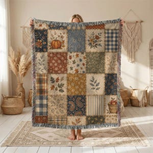 May include: A woven throw blanket featuring a patchwork design of various autumn-themed patterns, including pumpkins, fall leaves, floral motifs, plaid, and paisley prints in shades of orange, blue, green, and cream with a fringed edge.