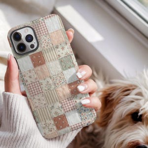 May include: A patchwork-style phone case featuring a variety of fabric patterns in soft, muted colors. The case has a mix of floral, striped, and gingham designs in shades of beige, pink, and green. The phone case is held in a person's hand.