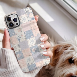 May include: A patchwork-style phone case featuring a mix of floral and gingham patterns in pastel pink, blue, and gray squares. The case has a camera cutout and a protective bumper. The overall design is reminiscent of a quilt.