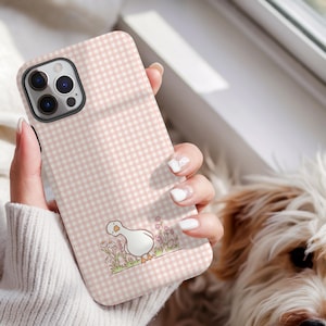 May include: Pink gingham phone case with a cartoon goose illustration. The case has a white and pink checkered pattern and a cute goose design with flowers. The phone case is designed to fit a smartphone.