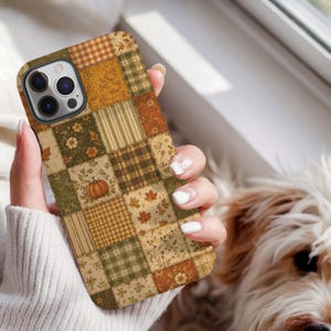 May include: A smartphone case featuring a patchwork design with various autumn-themed patterns including orange pumpkins, brown maple leaves, green and tan plaid, and floral motifs in shades of orange, brown, cream, and olive green.