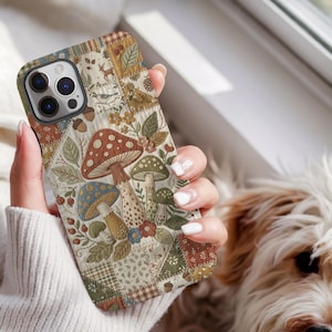 May include: A smartphone case featuring a patchwork design with various patterns including mushrooms, leaves, flowers, acorns, a deer, and a bird. The colour palette consists of muted earth tones like brown, green, cream, and blue with a quilted texture.