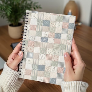 May include: A spiral-bound notebook featuring a patchwork quilt design on the cover. The pattern consists of small squares in muted shades of sage green, dusty pink, cream, and slate blue, displaying various floral, gingham, and polka dot prints.