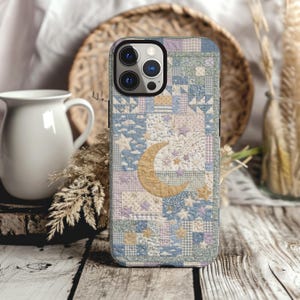May include: A smartphone case featuring a patchwork quilt design in soft shades of blue, lavender, and cream. The pattern includes small squares, stars, and a prominent golden crescent moon centered on the back, with a triple camera lens cutout.