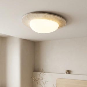 May include: A modern ceiling light fixture with a circular, textured, beige frame. The light has a rounded, opaque, white glass shade. The fixture is mounted on a white ceiling, providing ambient lighting.