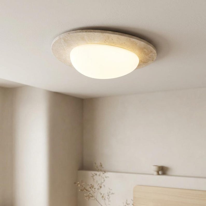 May include: A modern ceiling light fixture with a circular, textured, beige frame. The light has a rounded, opaque, white glass shade. The fixture is mounted on a white ceiling, providing ambient lighting.