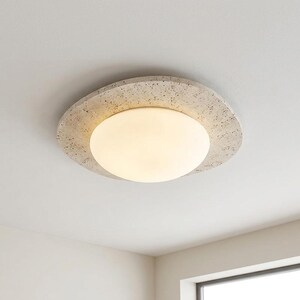 May include: A modern ceiling light fixture with a round, frosted glass shade and a textured, stone-like outer ring. The light emits a warm glow, and the fixture is mounted on a white ceiling.