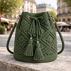 Può includere: Una borsa a secchiello all'uncinetto verde con un motivo a rombi. La borsa ha una chiusura con coulisse con nappe e hardware color oro. Anche la tracolla è verde e realizzata con lo stesso materiale della borsa.