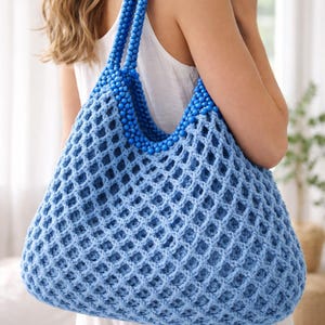 May include: A light blue crocheted tote bag with a beaded handle. The bag features a diamond-shaped net pattern and a rounded shape. The handle is made of small, round blue beads. The bag is held by a person wearing a white top.