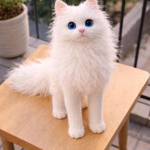 May include: A handcrafted white cat with striking blue eyes and a pink nose is positioned on a small wooden table. The cat features fluffy, textured fur and a long tail. The table is light brown and has four legs.