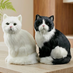 Può includere: Due realistiche statuette di gatto realizzate in morbida pelliccia sintetica. Un gatto è bianco tinta unita con occhi verdi e naso rosa. Il secondo gatto è bianco e nero con petto, segni sul viso e zampe bianche, occhi verdi e naso rosa.