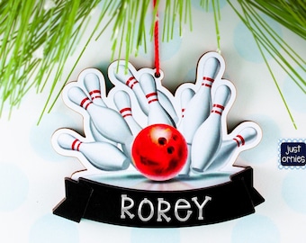 May include: Wooden bowling ornament featuring a red bowling ball striking white pins with red stripes. The ornament has a black banner with the name "ROREY" in silver lettering. A red string is attached for hanging.