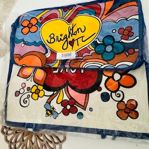 Op de afbeelding: Een kleurrijke draagtas met een retro-ontwerp. De tas heeft een groot geel hart met de tekst "Brighton TC" en een rood hart. Het ontwerp bevat bloemen, krullen en het woord "LOVE". De tas is verpakt in doorzichtig plastic.