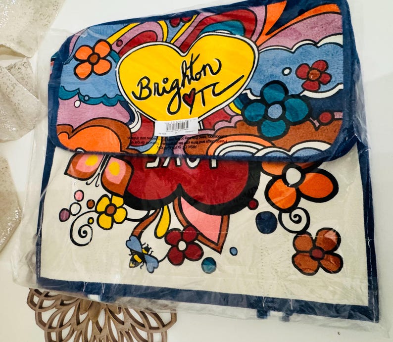 Op de afbeelding: Een kleurrijke draagtas met een retro-ontwerp. De tas heeft een groot geel hart met de tekst "Brighton TC" en een rood hart. Het ontwerp bevat bloemen, krullen en het woord "LOVE". De tas is verpakt in doorzichtig plastic.