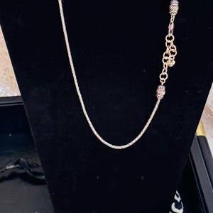 May include: A silver-toned necklace with a delicate chain and decorative beads. The necklace is displayed on a black velvet background. The necklace is part of a jewelry collection.
