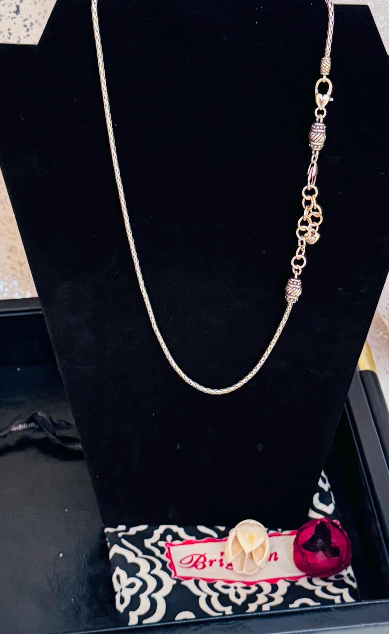 May include: A silver-toned necklace with a delicate chain and decorative beads. The necklace is displayed on a black velvet background. The necklace is part of a jewelry collection.