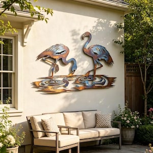 May include: Metal wall art showing two flamingo sculptures in blue and copper tones. The flamingos are set in a pond scene, mounted on a cream wall. This artwork provides a nature-inspired decorative element for an outdoor area.