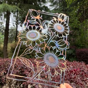 May include: A decorative metal art piece featuring a sunflower design. The artwork is cut from iridescent metal, displaying a range of colors. The sunflowers are framed within a rectangular border, suitable for garden or home decor.