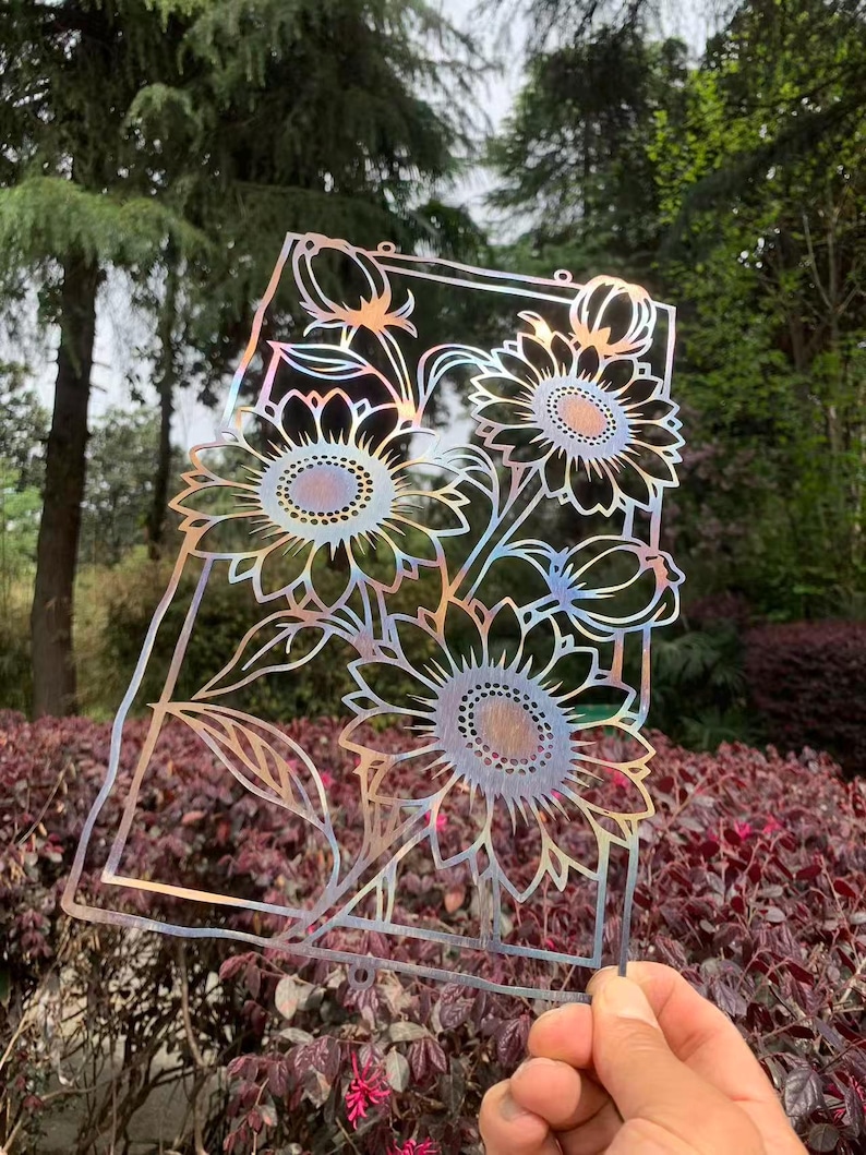 May include: A decorative metal art piece featuring a sunflower design. The artwork is cut from iridescent metal, displaying a range of colors. The sunflowers are framed within a rectangular border, suitable for garden or home decor.