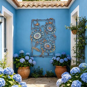 May include: A courtyard with a blue wall featuring a metal sunflower wall art. Large terracotta pots hold blue hydrangea plants. The courtyard has a stone pathway and a terracotta tile roof.