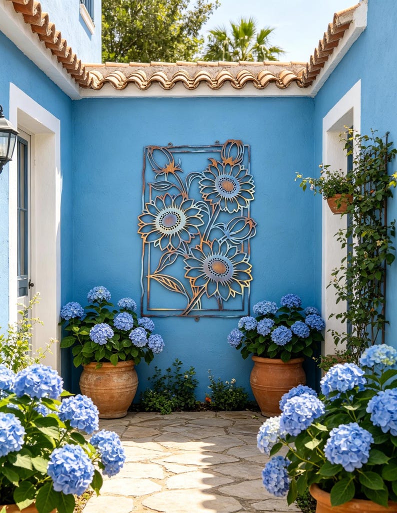 May include: A courtyard with a blue wall featuring a metal sunflower wall art. Large terracotta pots hold blue hydrangea plants. The courtyard has a stone pathway and a terracotta tile roof.