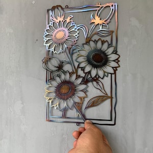 May include: Metal wall art featuring sunflowers in a rectangular frame. The sunflowers have detailed petals and textured centers, with a mix of bronze, gold, and blue hues. The piece is designed to be mounted on a wall.