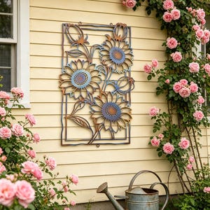 May include: A metal wall art piece featuring sunflowers with blue and brown accents. The artwork is rectangular and mounted on a yellow wall. A vintage watering can sits below the art, surrounded by pink roses.