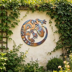 Puede incluir: Una pieza de arte mural de metal con un diseño estilizado de lagarto en tonos cobre, azul y bronce. El lagarto está rodeado por un anillo decorativo, montado en una pared crema y rodeado de exuberante vegetación, creando una estética de jardín.