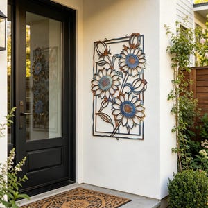 May include: A metal sunflower wall art piece with a rectangular frame. The sunflowers have blue and brown accents. The art is mounted on a white wall next to a black door and a decorative doormat.
