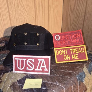 May include: Black baseball cap with a square patch and six metal eyelets. Three rectangular patches with text: "USA", "QUESTION EVERYTHING", and "DONT TREAD ON ME". Patches are red and yellow with white lettering.