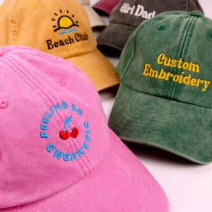 Könnte beinhalten: Eine Auswahl an Baseballkappen in verschiedenen Farben mit gestickten Designs. Die Kappen sind in Rosa, Gelb und Grün gehalten. Eine rosa Kappe trägt den Schriftzug "Feeling So Cherry" mit einer Kirschgrafik. Eine gelbe Kappe hat eine Sonne und den Text "Beach Club". Eine grüne Kappe trägt "Custom Embroidery".