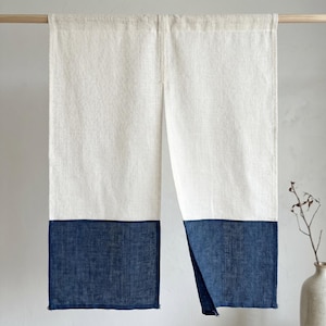 May include: A split-panel curtain made of off-white linen fabric with a deep navy blue colour-blocked section at the bottom. The curtain hangs from a wooden rod and features a vertical slit down the centre, creating two distinct fabric panels.
