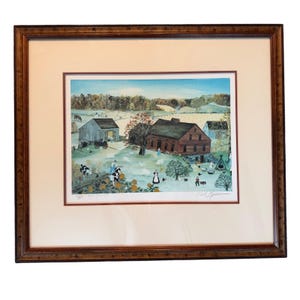 May include: Framed print of a rural farm scene with a red house, barns, and figures. The artwork features a brown wooden frame and a cream-colored mat. The scene includes cows, sheep, and a blue sky.