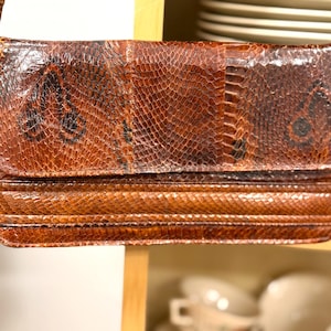 May include: A vintage brown snakeskin handbag with a shoulder strap. The bag features a rectangular shape with a flap closure and a textured, scaly pattern. The color is a mix of brown and tan.