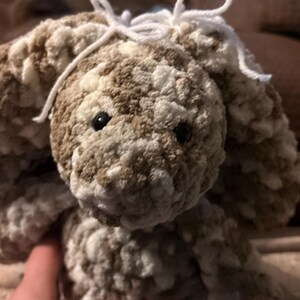 Op de afbeelding: Een handgemaakt, pluche konijn in bruin- en wittinten. Het konijn heeft lange, slappe oren, zwarte ogen en een witte garenstrik. Het zachte, getextureerde materiaal geeft het een knuffelbaar uiterlijk. Het konijn is een knuffel.