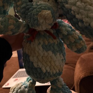 Op de afbeelding: Een handgemaakt pluchen konijn in tinten blauw, wit en geel. Het konijn heeft lange floppy oren, een kleine rode strik en een zacht, getextureerd uiterlijk. Dit knuffelige speelgoed is perfect voor kinderen.
