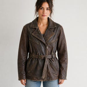 May include: A brown leather jacket with a belted waist and a zipper closure. The jacket has a classic biker style with a notched collar and multiple pockets. The leather has a distressed look, giving it a vintage appearance.