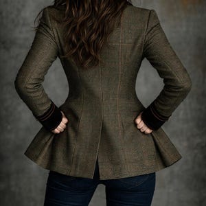 Pu&ograve; includere: Giacca in tweed verde oliva con peplo svasato. Presenta un sottile motivo a quadri, polsini in velluto scuro e uno spacco sulla schiena. La persona indossa jeans blu scuro.