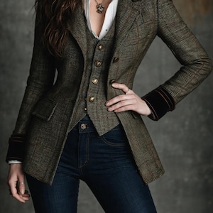 Pu&ograve; includere: Un completo in tweed a tre pezzi nei toni del verde e del marrone, con una giacca con colletto e polsini in velluto nero, un gilet abbinato e jeans blu scuro. La giacca ha bottoni dorati e un design classico.