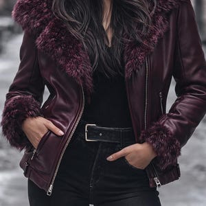 May include: Burgundy faux leather jacket with a faux fur collar and cuffs. The jacket has a zipper closure and a black belt. The model is wearing black jeans and a black top. The jacket is a stylish outerwear option.